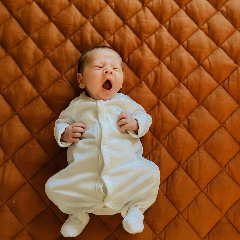 Tarçın renkli kapitone oyun halısı üzerinde yatan yenidoğan bebek
