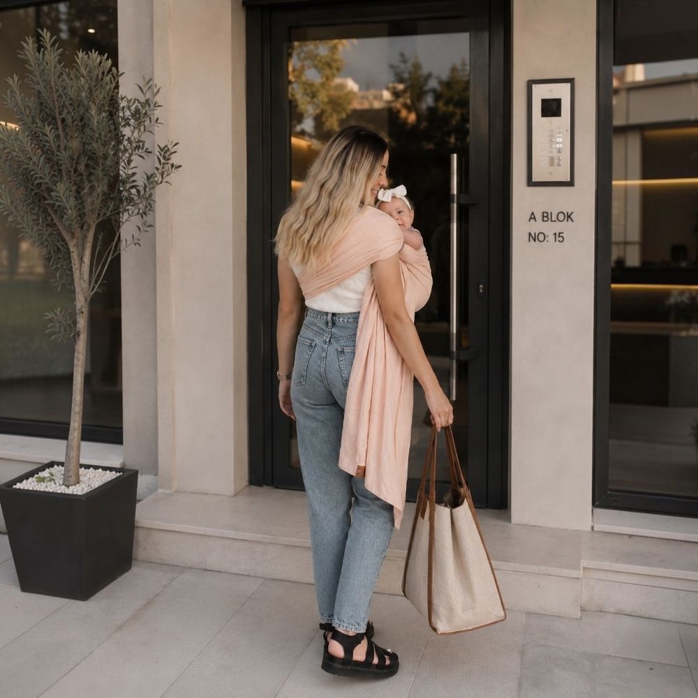 Balküpü Studio halka sling ile bebeğini taşıyarak evden çıkan anne. Bebek taşıma slingi sayesinde eller serbest kalırken anne günlük yaşamına daha rahat devam edebilir, bebeğine yakın kalırken kendini daha özgür hissedebilir.