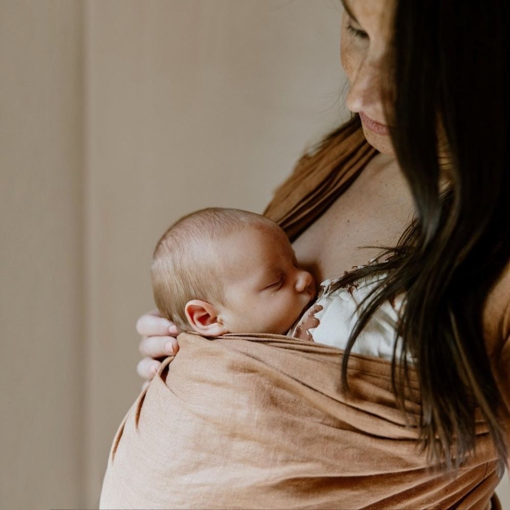 %100 keten halka sling içinde ergonomik M pozisyonunda taşınan yenidoğan bebek ve annesi. Güvenli, konforlu ve doğru halka sling seçimini gösteren yakın plan kullanım görseli.