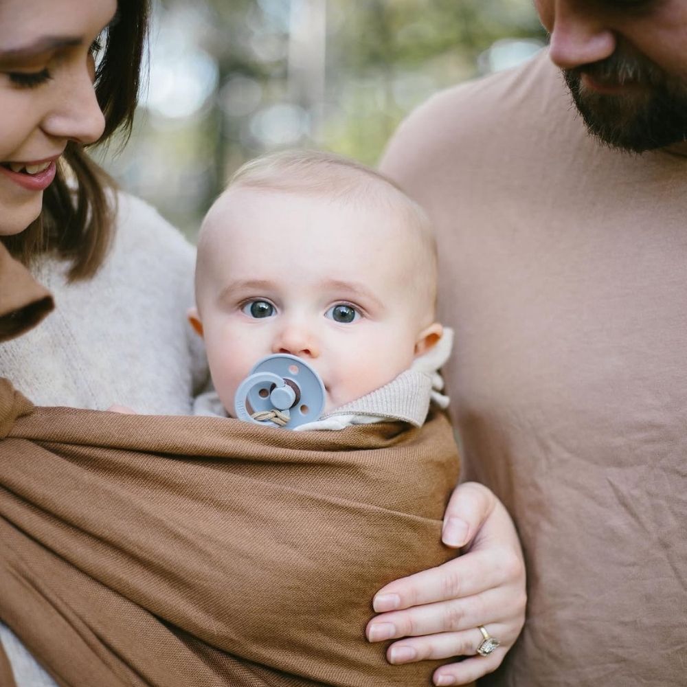 Halka sling içinde bebeğini güvenle taşıyan anne ve yanında destek veren baba. İlk kez anne olan aileler için güvenli, konforlu ve ergonomik bebek taşıma deneyimini gösteren yaşam fotoğrafı.